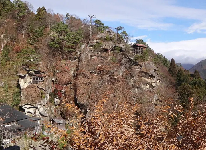 A sheer rock cliff with autumn trees and a small temple hall