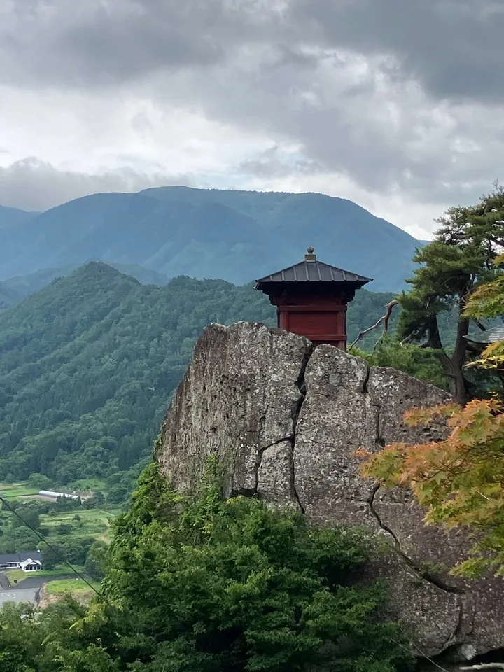 A small red temple hall perched on a rock outcrop among trees